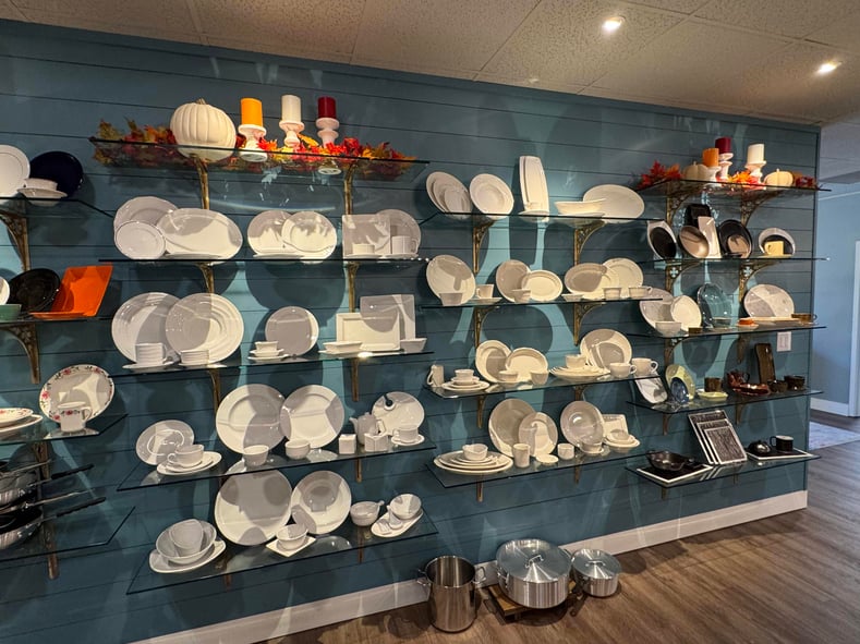 Blue wood wall holds multiple shelves of white dinnerware in Lindox Siegel Baker Culinary Club test kitchen