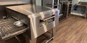 View of conveyor oven on brown wood floor with other equipment to the right